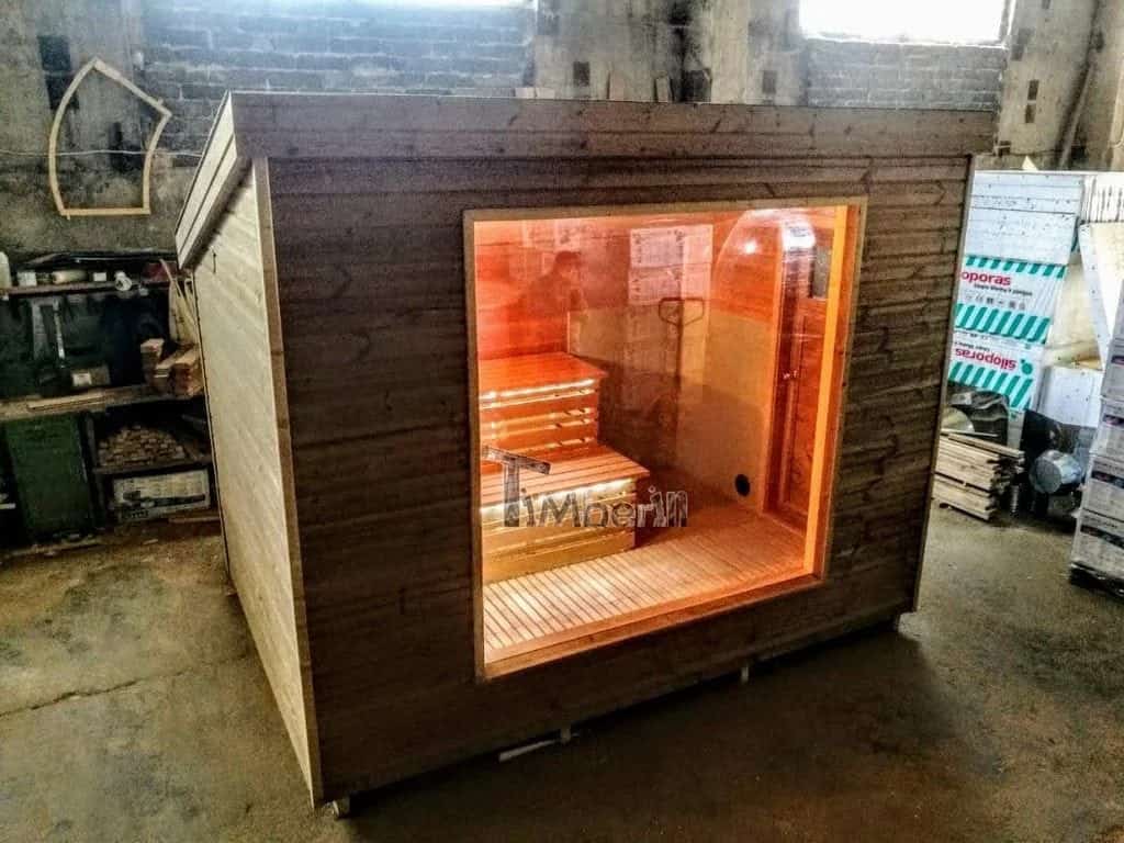 Sauna extérieur moderne en bois avec grande baie vitrée et éclairage chaleureux exposé dans un atelier.