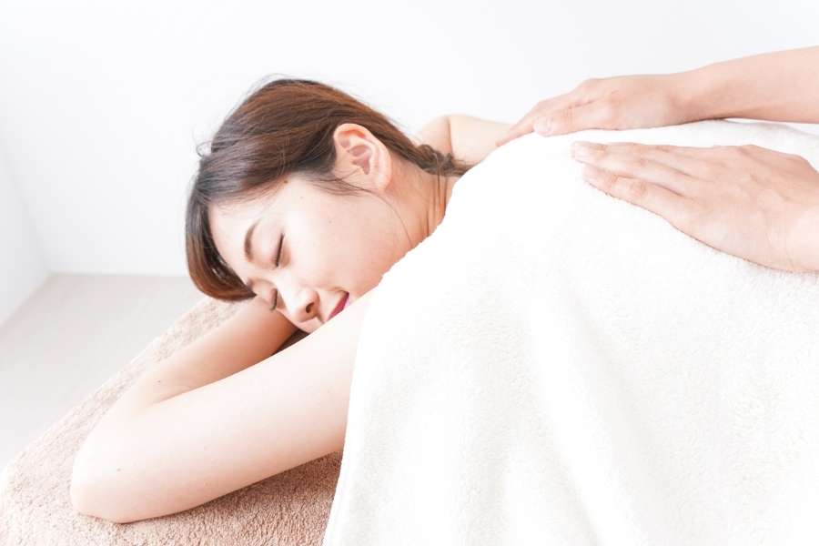 Jeune femme détendue recevant un massage du dos par un praticien dans une ambiance de spa lumineuse.